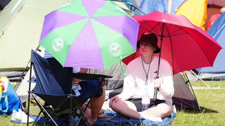 Spectators shield themselves from the sun with umbrellas in the Wimbledon queue